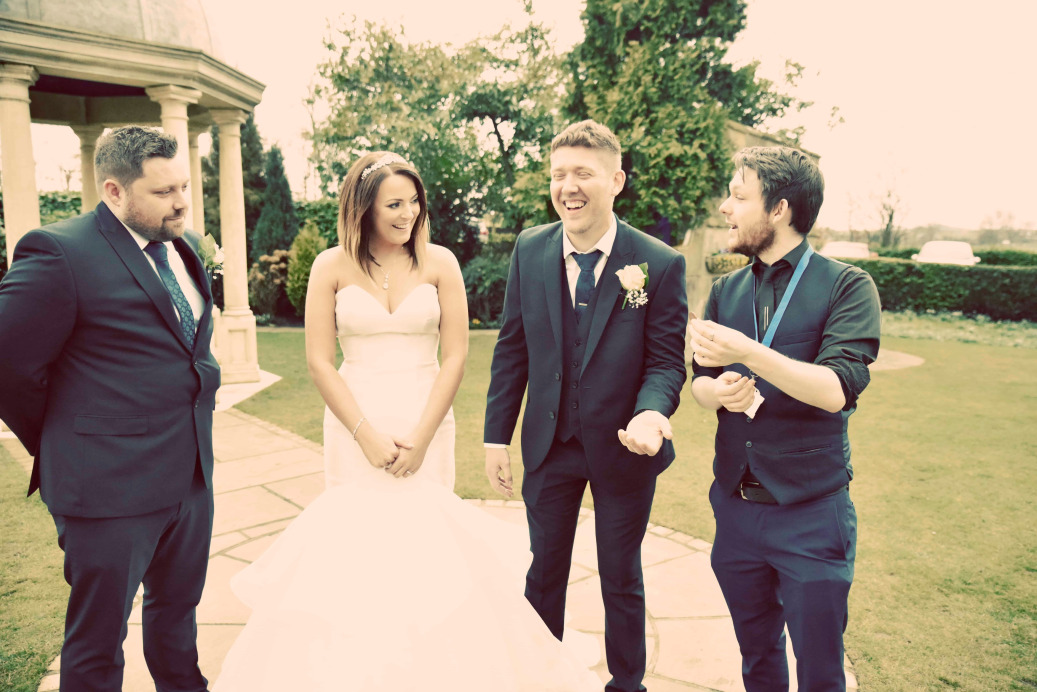 Wedding magician Greg Holroyd performing for newlyweds outdoors—guests laughing in amazement during a close-up illusion.
