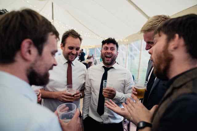 Greg Holroyd performing magic for a group of men in suits at a marquee corporate party, causing laughter and amazement