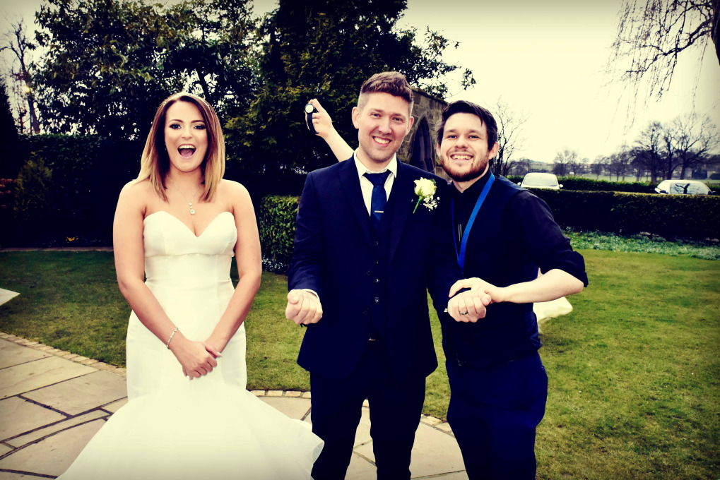 Bride and groom laughing as magician Greg Holroyd reveals he’s secretly stolen the groom’s watch—crowd loses it during the big wedding-day reveal