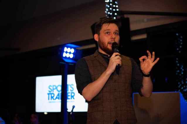 Greg Holroyd speaking at a Sport Traider corporate event, holding a microphone and engaging the crowd on stage