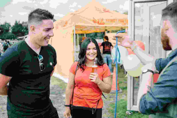 "Greg Holroyd performing rope magic at a summer corporate party, guests laughing and holding drinks under a yellow branded marquee"