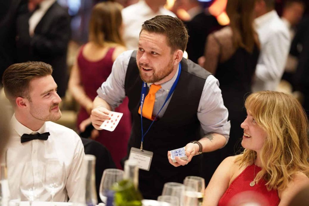 Greg Holroyd performing close-up magic at a formal event, amazing guests with a card trick at the dinner table.