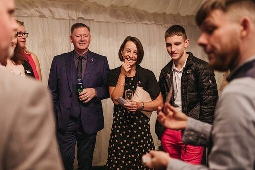"Greg Holroyd performing a magic routine for a group of guests at a corporate event, with smiling faces and hands mid-trick"