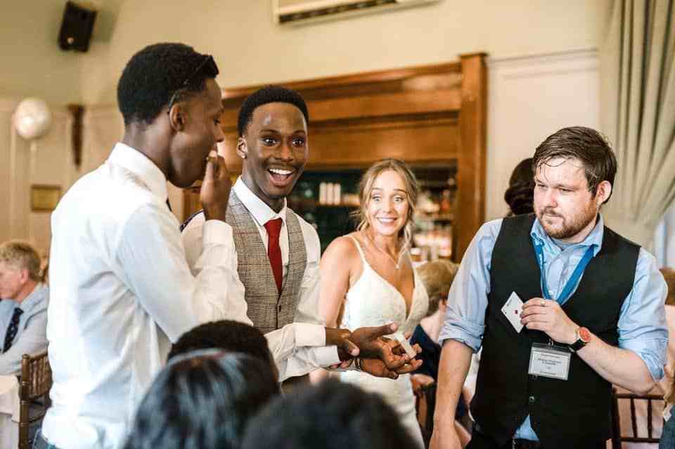 Wedding magician Greg Holroyd shocks guests with a killer card reveal—groom squad in awe, bride left speechless mid-laugh.